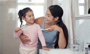 a parent brushing their teeth with their child