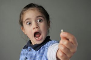 Girl with blue striped shirt holding out a lost tooth with a shocked expression