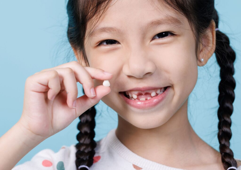 Little girl in pigtails smiling holding up lost tooth