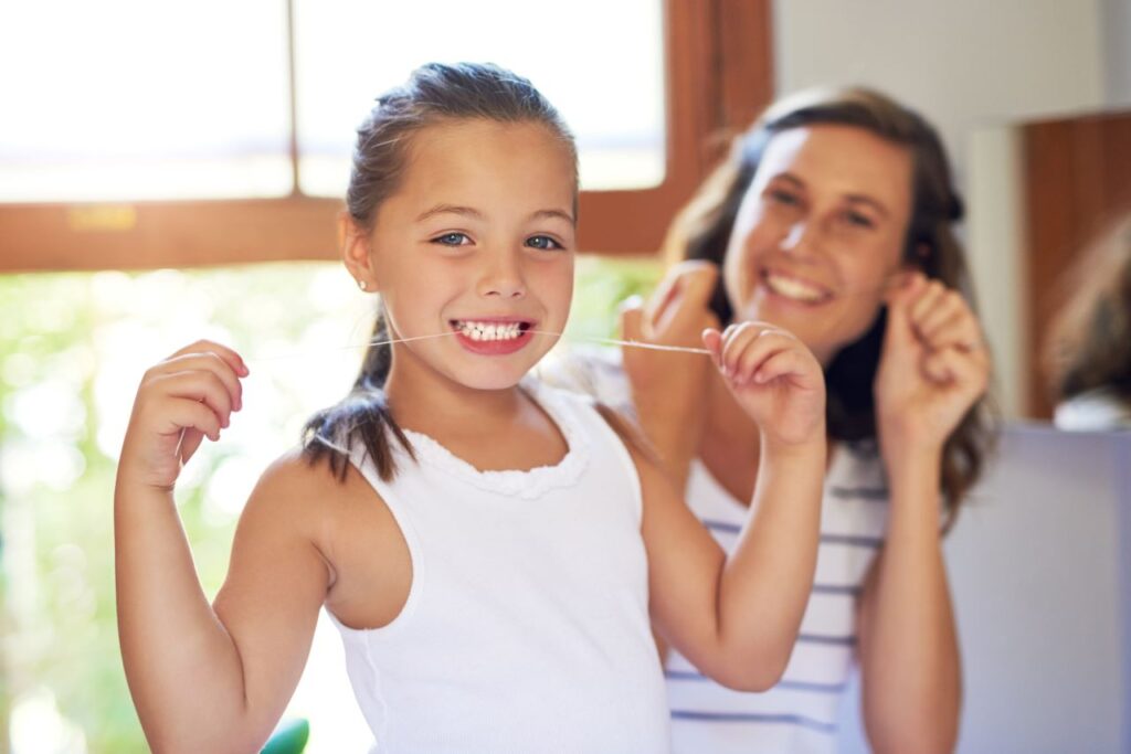 A little girl flossing her teeth with her mother